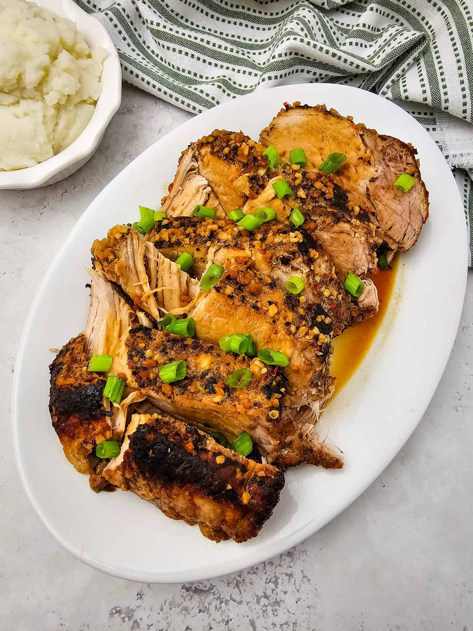 Sliced Honey Garlic Pork Roast topped with chopped green onions on a white plate, served alongside creamy mashed potatoes.