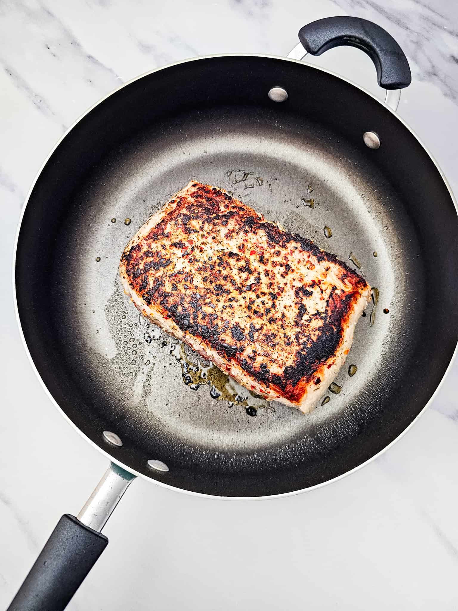 A piece of seared salmon cooking in a nonstick frying pan on a marble countertop, next to a Crockpot ready for making Honey Garlic Pork Roast.