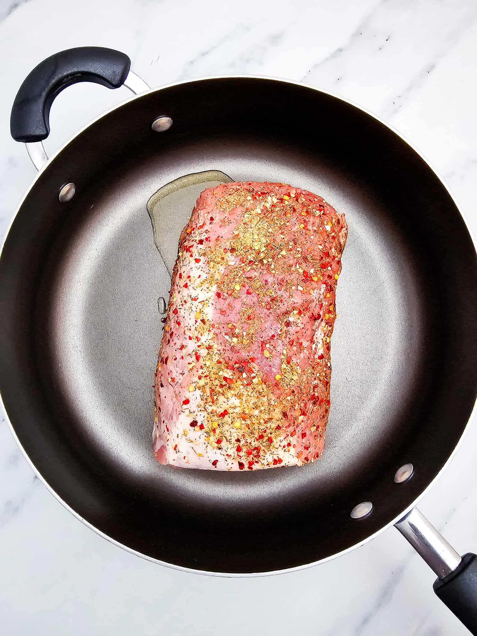Honey Garlic Pork Roast seasoned to perfection in a black pan with a bay leaf, resting on a white marble surface.