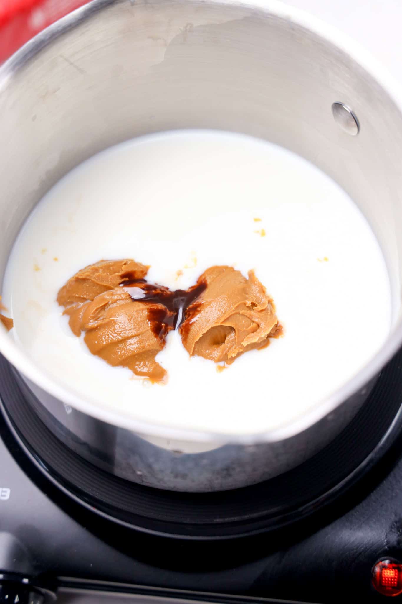 A saucepan with milk, peanut butter, vanilla extract, and Biscoff Hot Chocolate on a stovetop, ready to be mixed.
