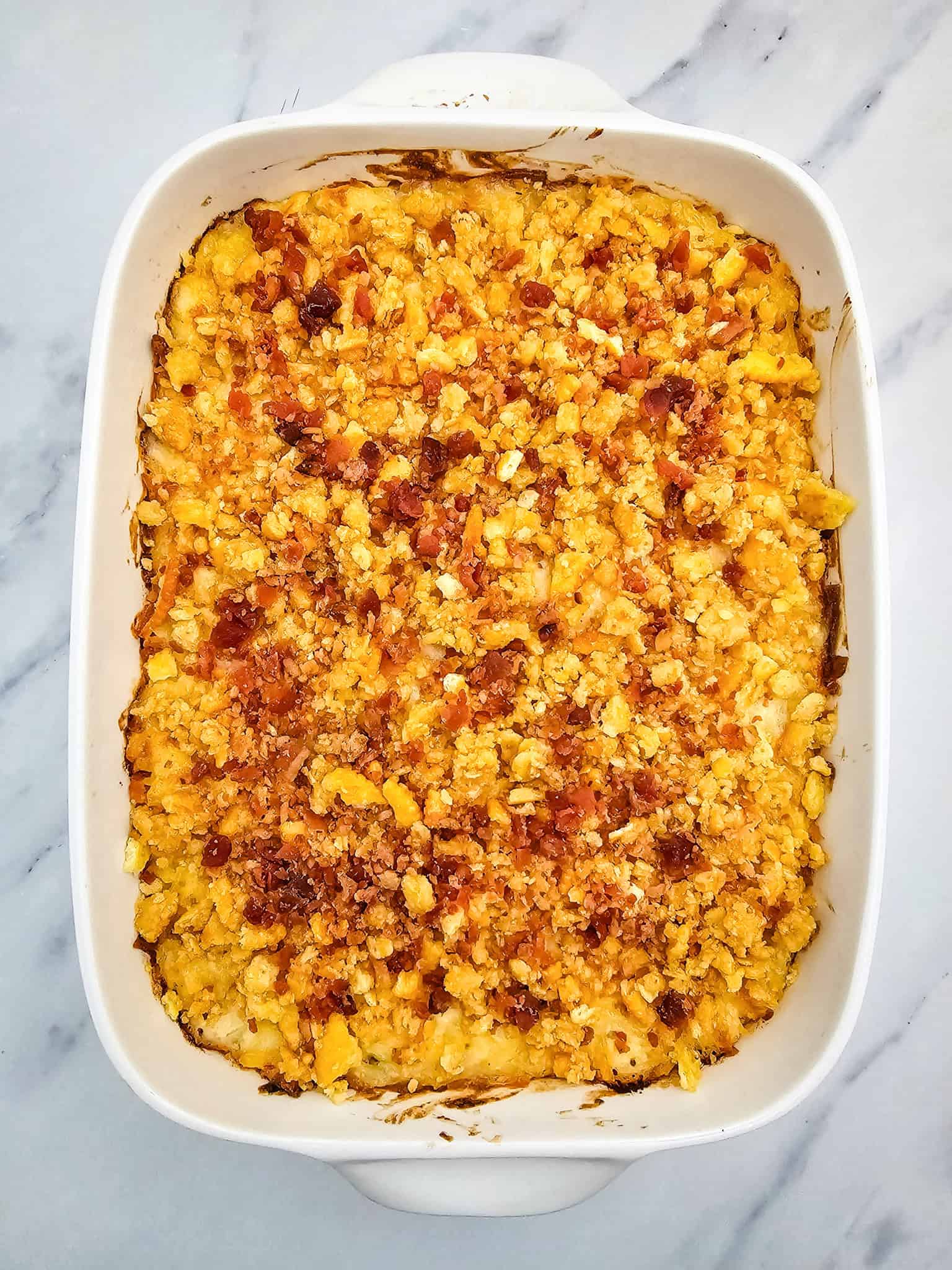 Baked cheesy casserole with a golden, crispy topping in a white dish on a marble surface.