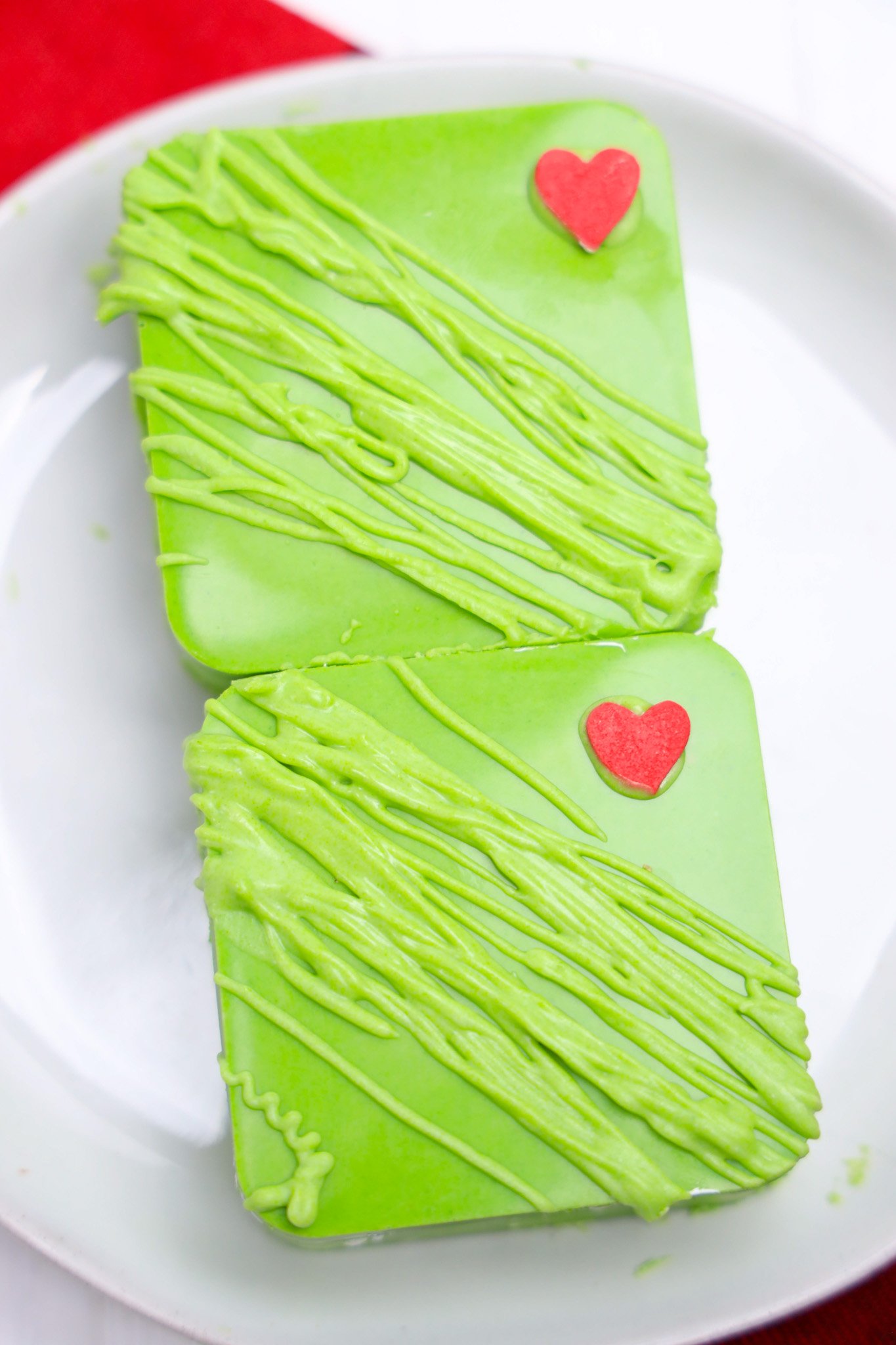 Two green square Grinch S'mores Bars with green drizzle and red heart decorations, served on a white plate.