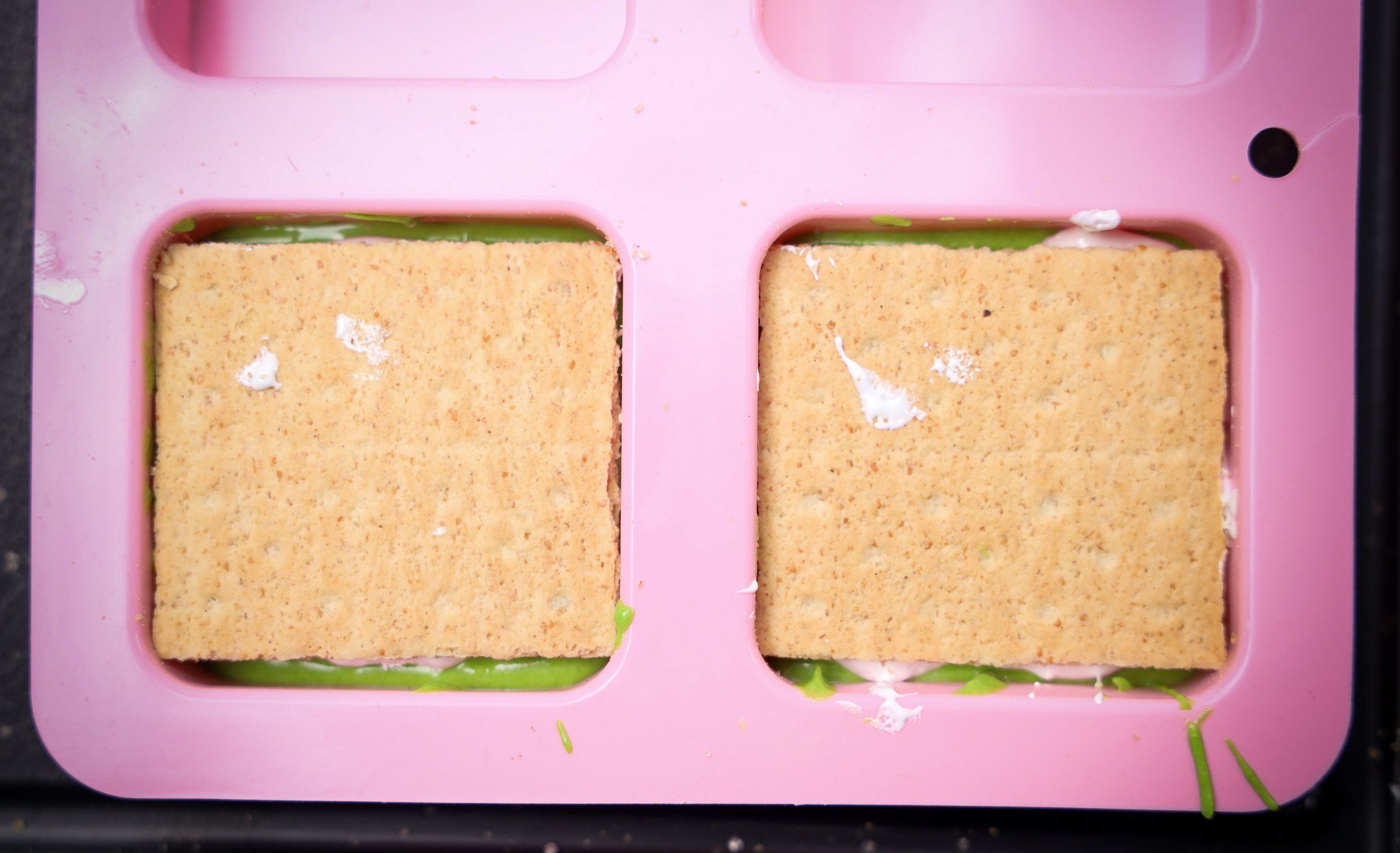 Two graham crackers in a pink silicone mold, with green and white filling peeking around the edges