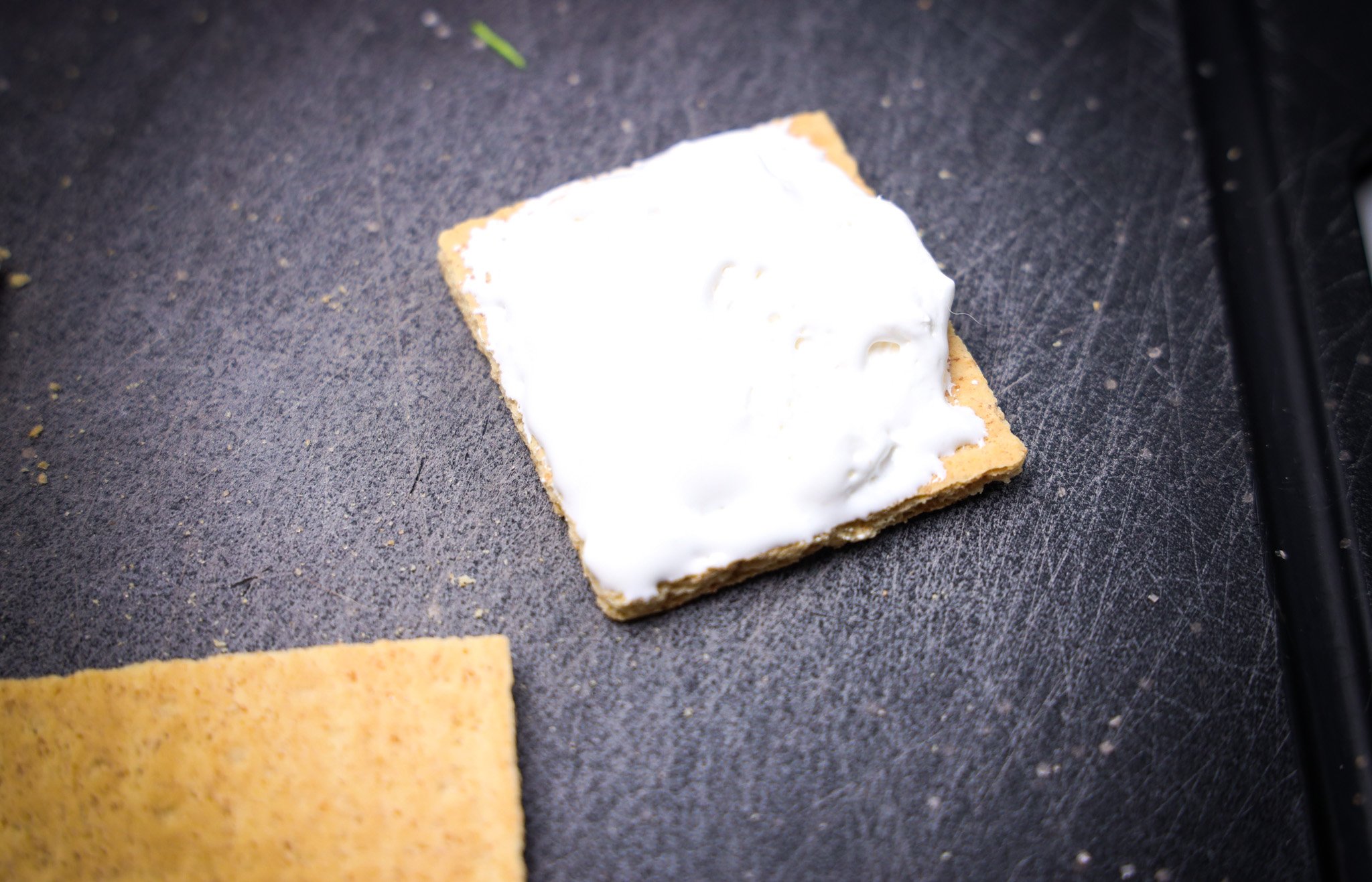 A graham cracker topped with a layer of marshmallow fluff on a dark surface