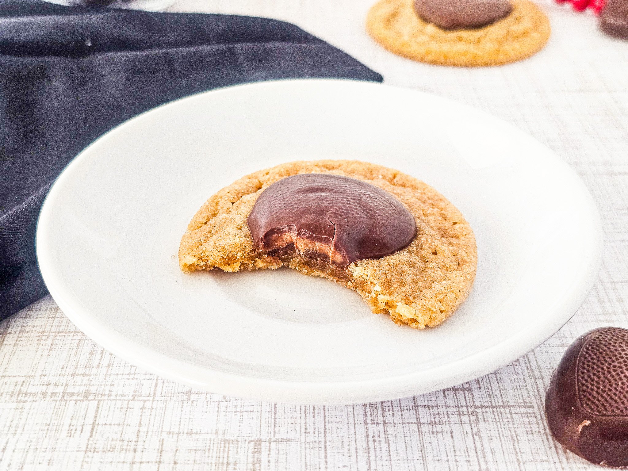 A Peanut Butter Blossoms cookie with a chocolate center and a bite taken out, on a white plate.
