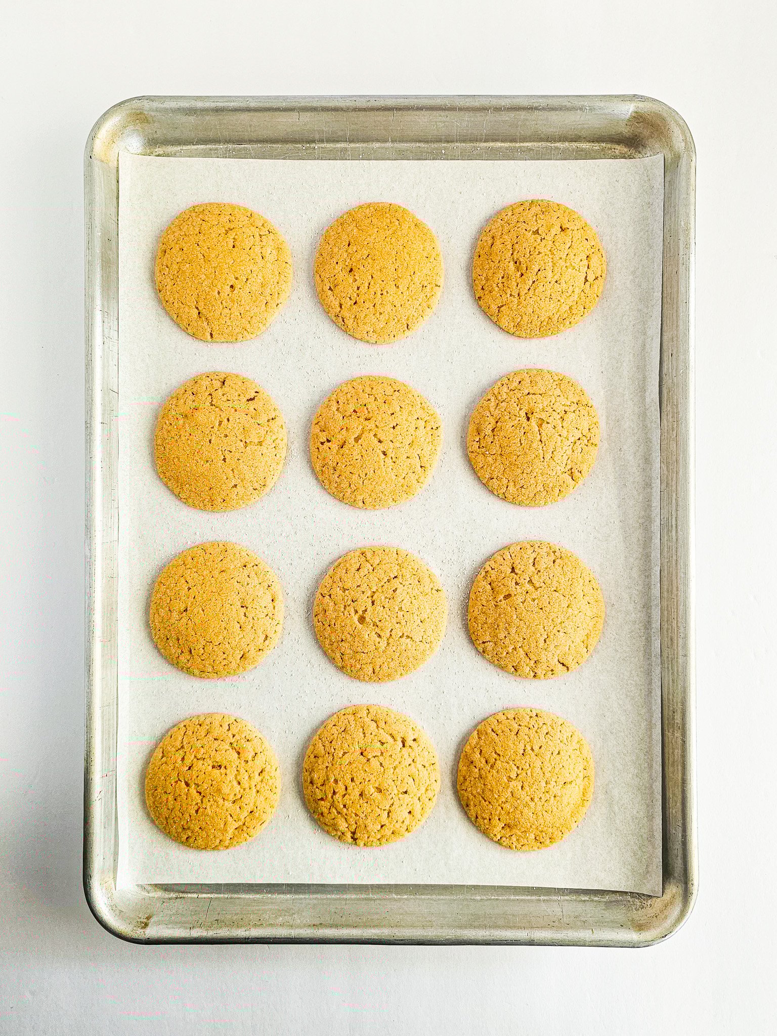 A baking tray with twelve round, golden-brown Easy Peanut Butter Blossoms sits on parchment paper.