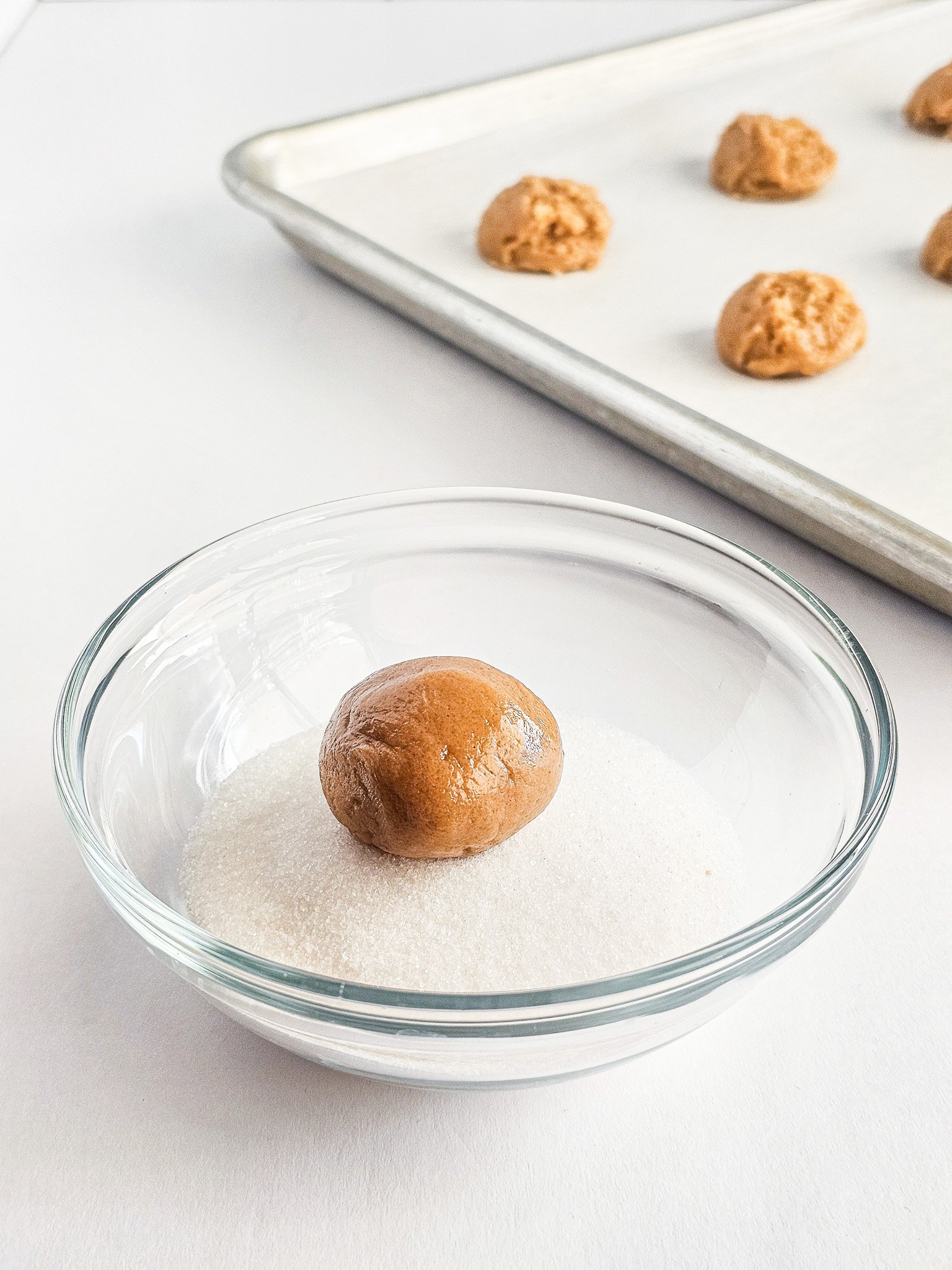 A cookie dough ball in sugar, with more Easy Peanut Butter Cookies waiting on a baking tray in the background.