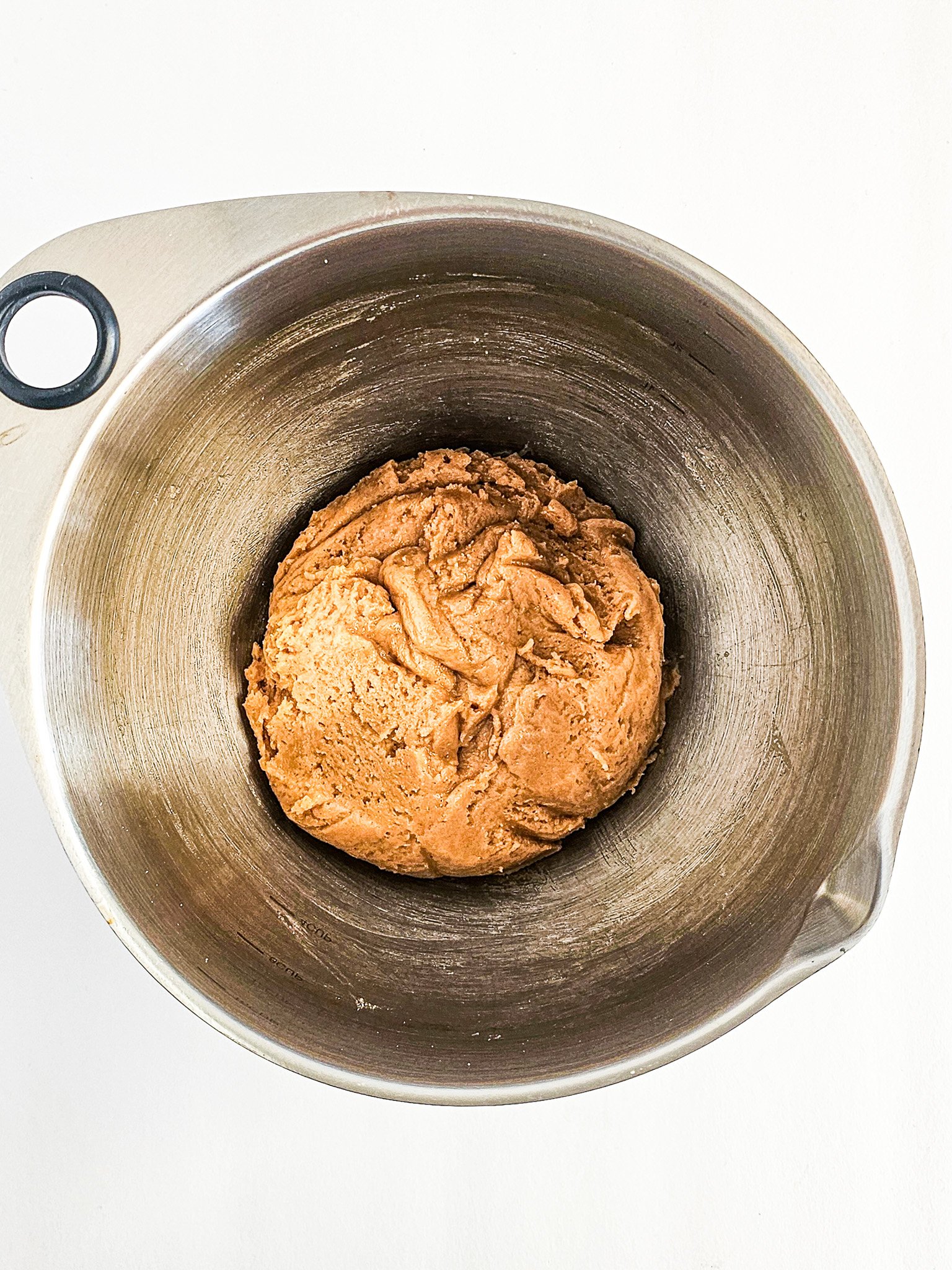 A ball of brown dough for Easy Peanut Butter Cookies rests in a metal mixing bowl on a white background.