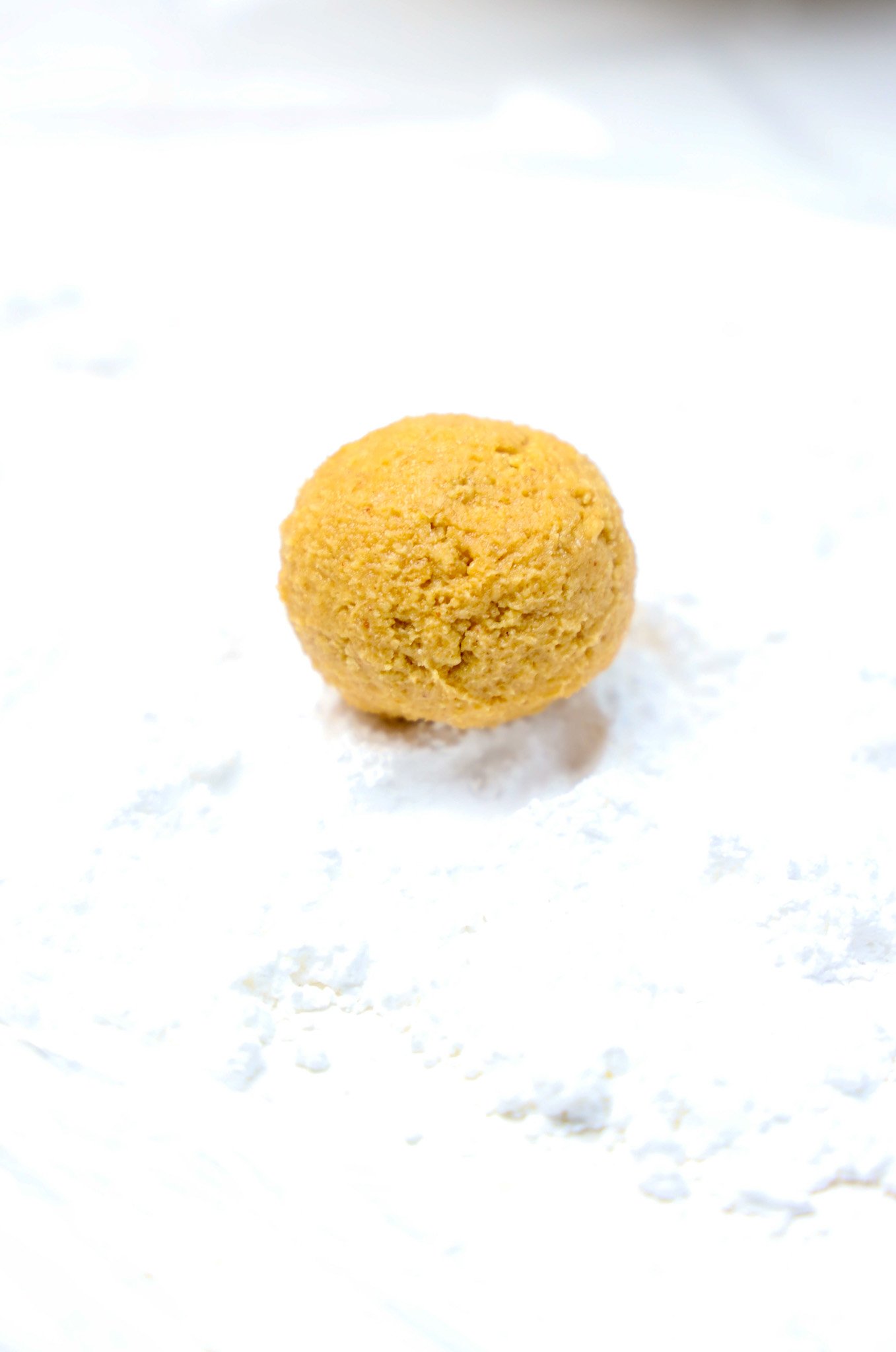 A single round Peanut Butter Snowball sits on a white, powdery surface, ready to be enjoyed.