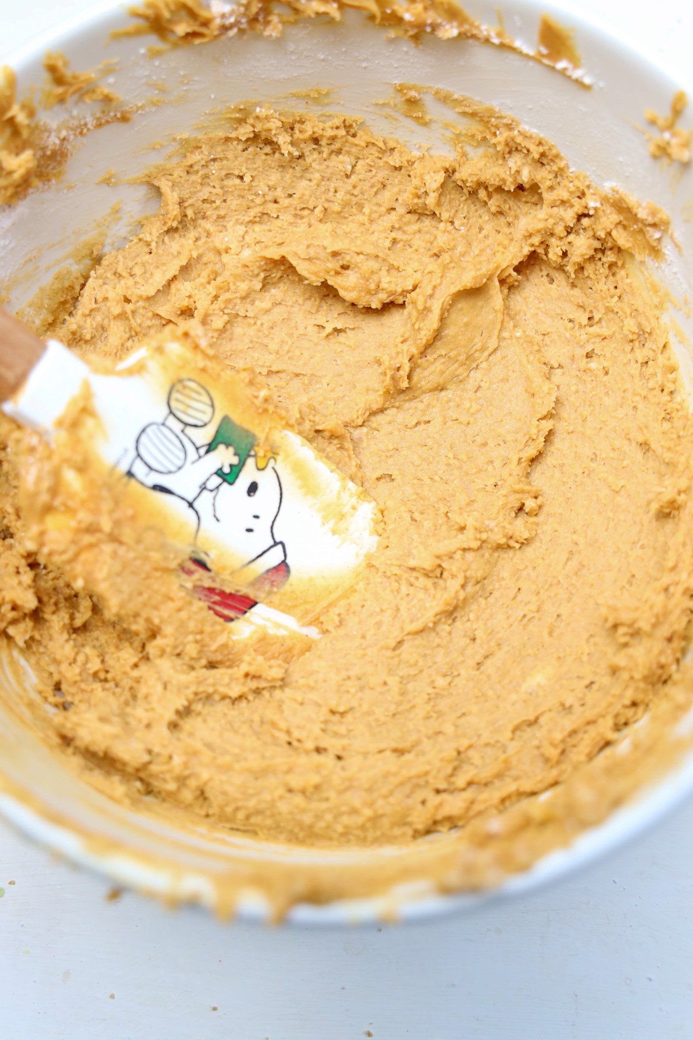 Creamy cookie dough in a bowl with a spatula featuring a Christmas-themed cartoon character, perfect for making festive Peanut Butter Snowballs.