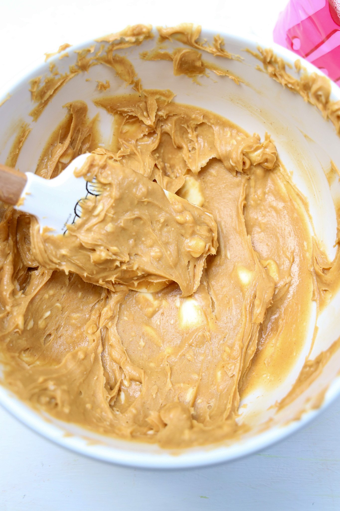 Creamy cookie dough being mixed in a white bowl with a spatula, showing chunks of butter-perfect for making irresistible Peanut Butter Snowballs.