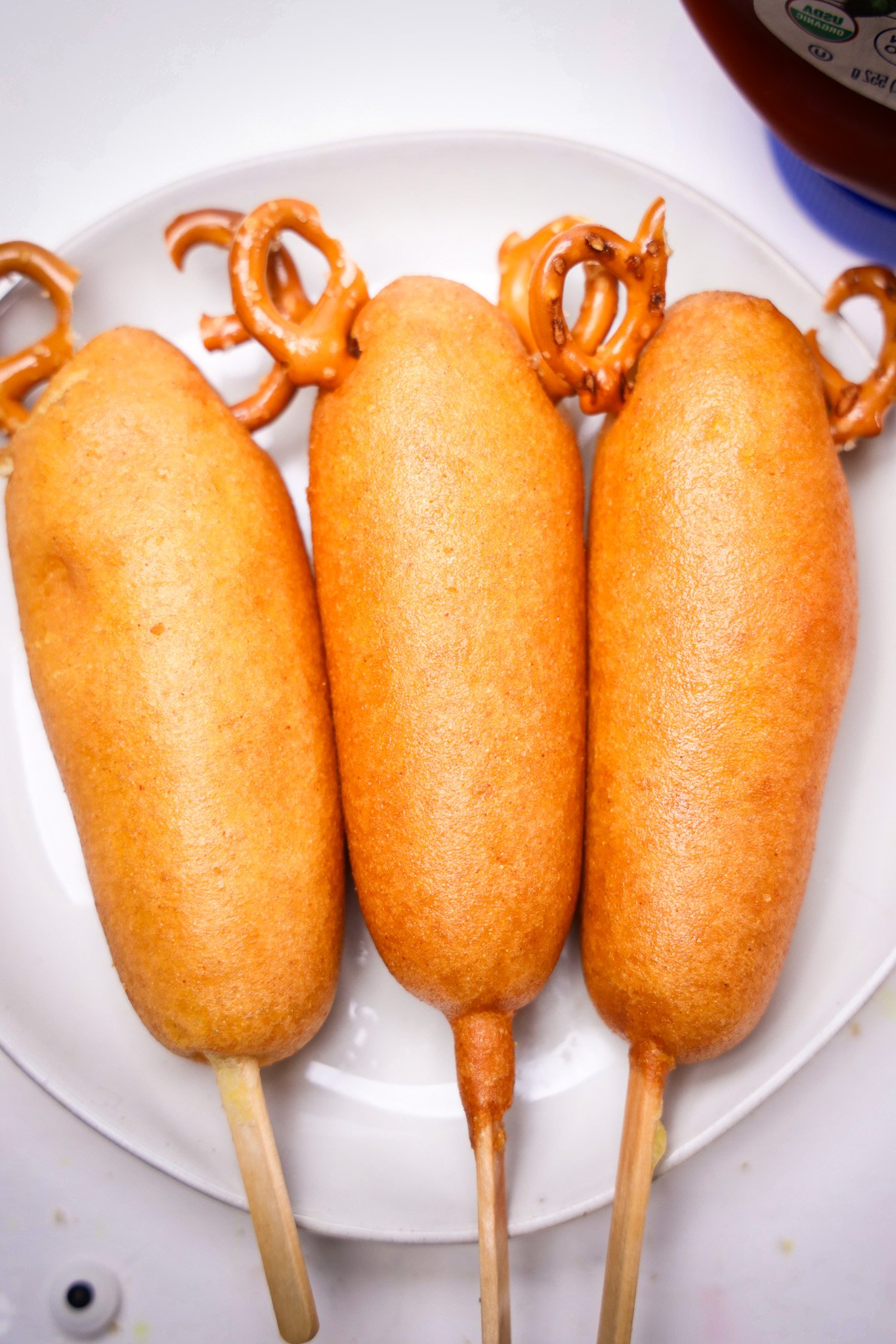 Three Corn Dogs on sticks with pretzel twists attached to the top, arranged on a white plate, create a fun and festive Rudolph-inspired snack.