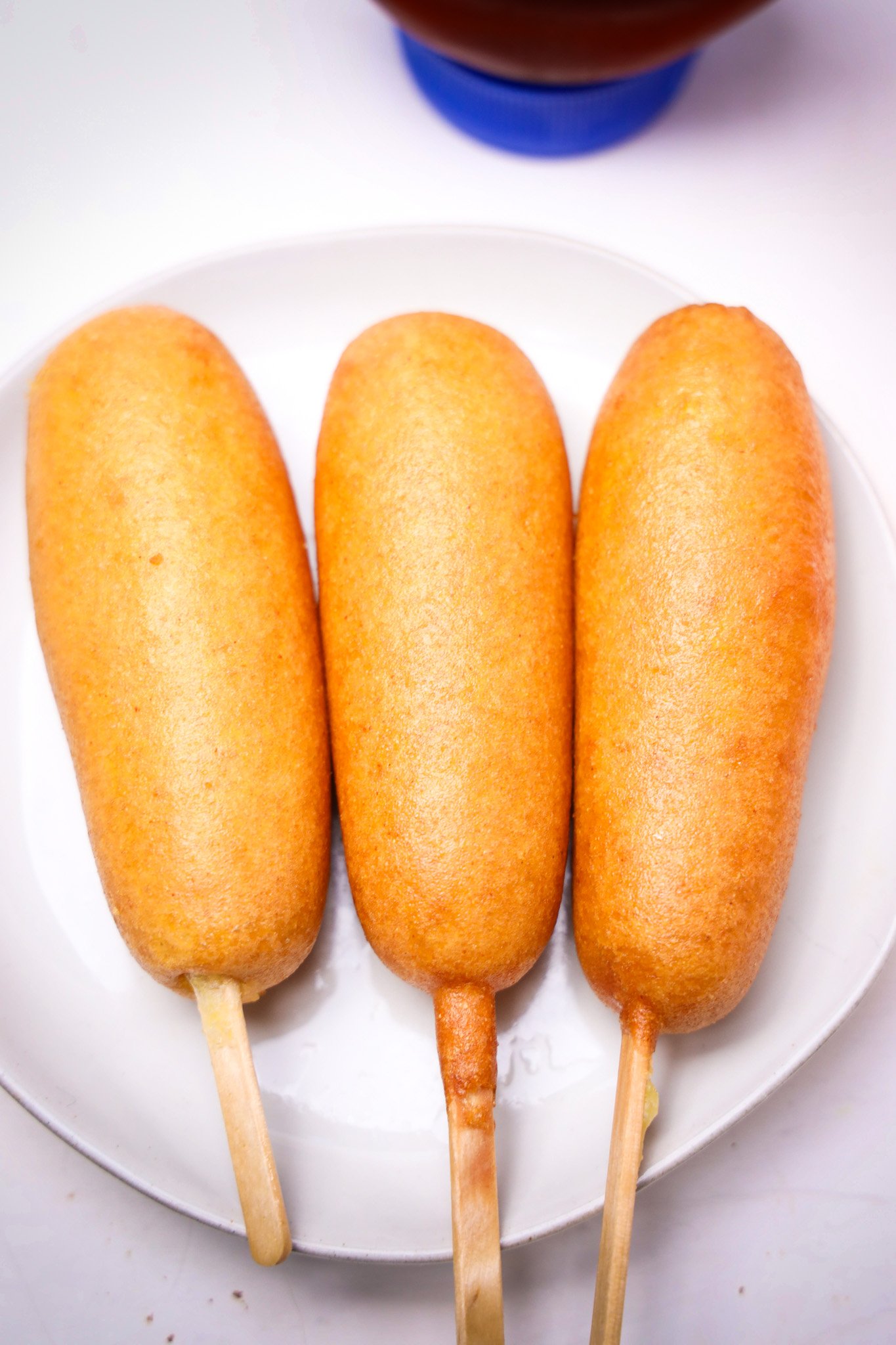 Three Corn Dogs on wooden sticks are arranged side by side on a white plate, ready to enjoy—perfect for sharing at your next Rudolph-themed gathering.