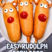 Three Rudolph Corn Dogs decorated as Rudolph with pretzel antlers, candy eyes, and ketchup noses are served on a white plate—festive and fun for any holiday gathering.