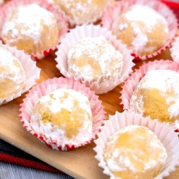 Peanut Butter Snowballs coated in powdered sugar sit in paper cups, beautifully arranged on a wooden board.