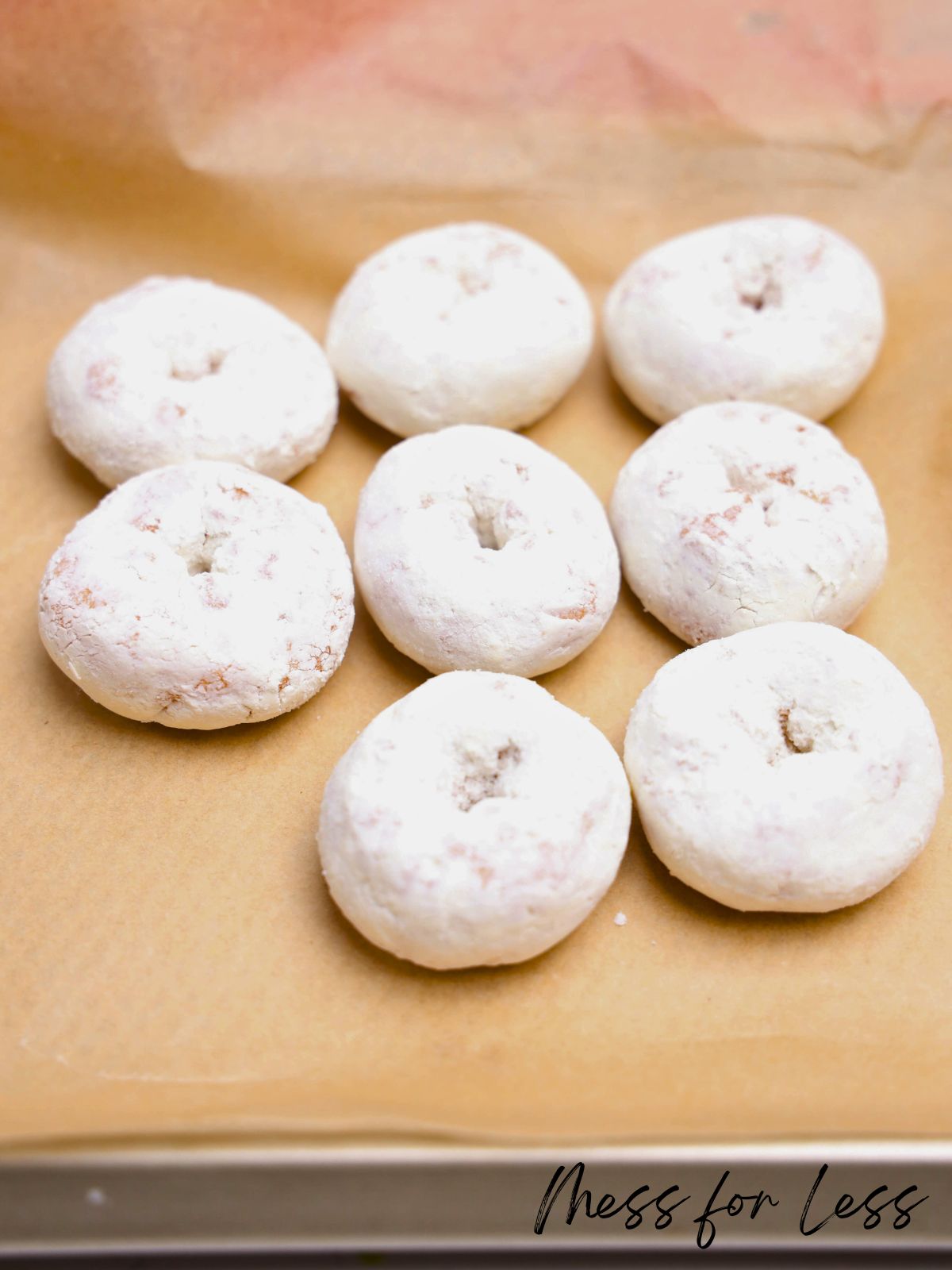 Seven powdered sugar donuts are arranged on brown parchment paper