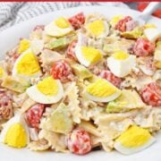 Cobb Pasta Salad featuring bowtie pasta, chopped hard-boiled eggs, cherry tomatoes, avocado, and creamy dressing served on a white plate.