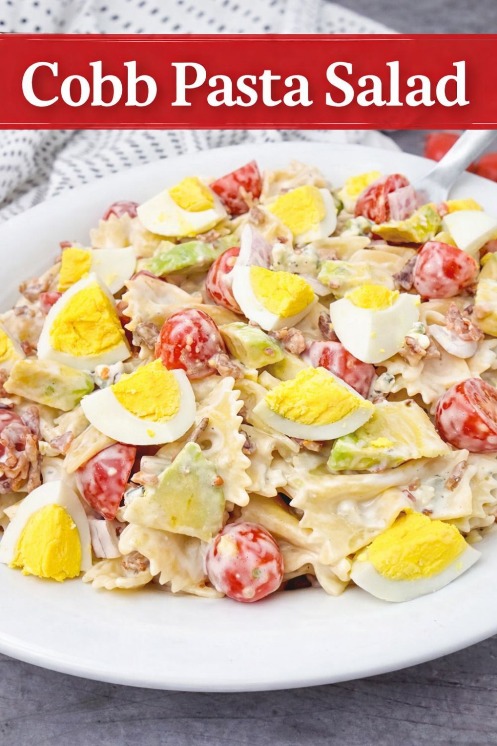 Cobb Pasta Salad featuring bowtie pasta, chopped hard-boiled eggs, cherry tomatoes, avocado, and creamy dressing served on a white plate.