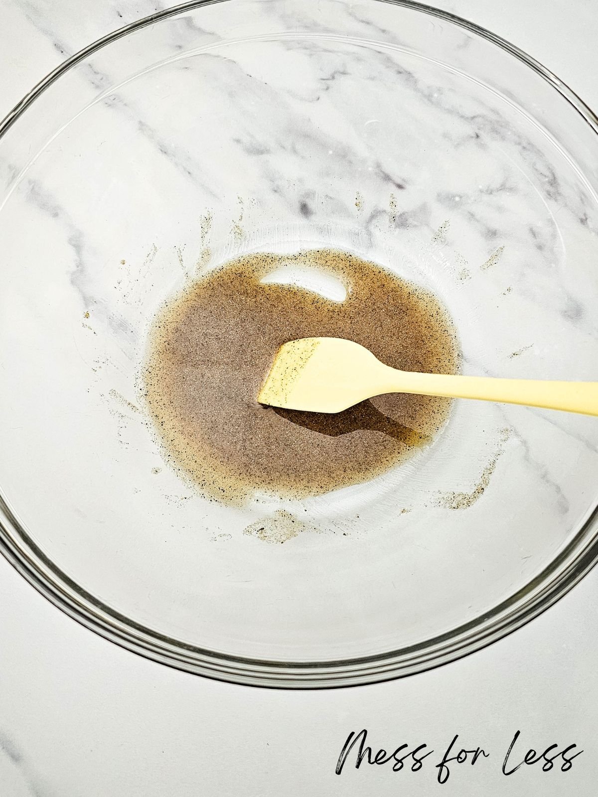A glass bowl with a brown liquid and a spatula sits on a white countertop, ready to coat sheet pan veggies and sausage for an easy, flavorful meal.