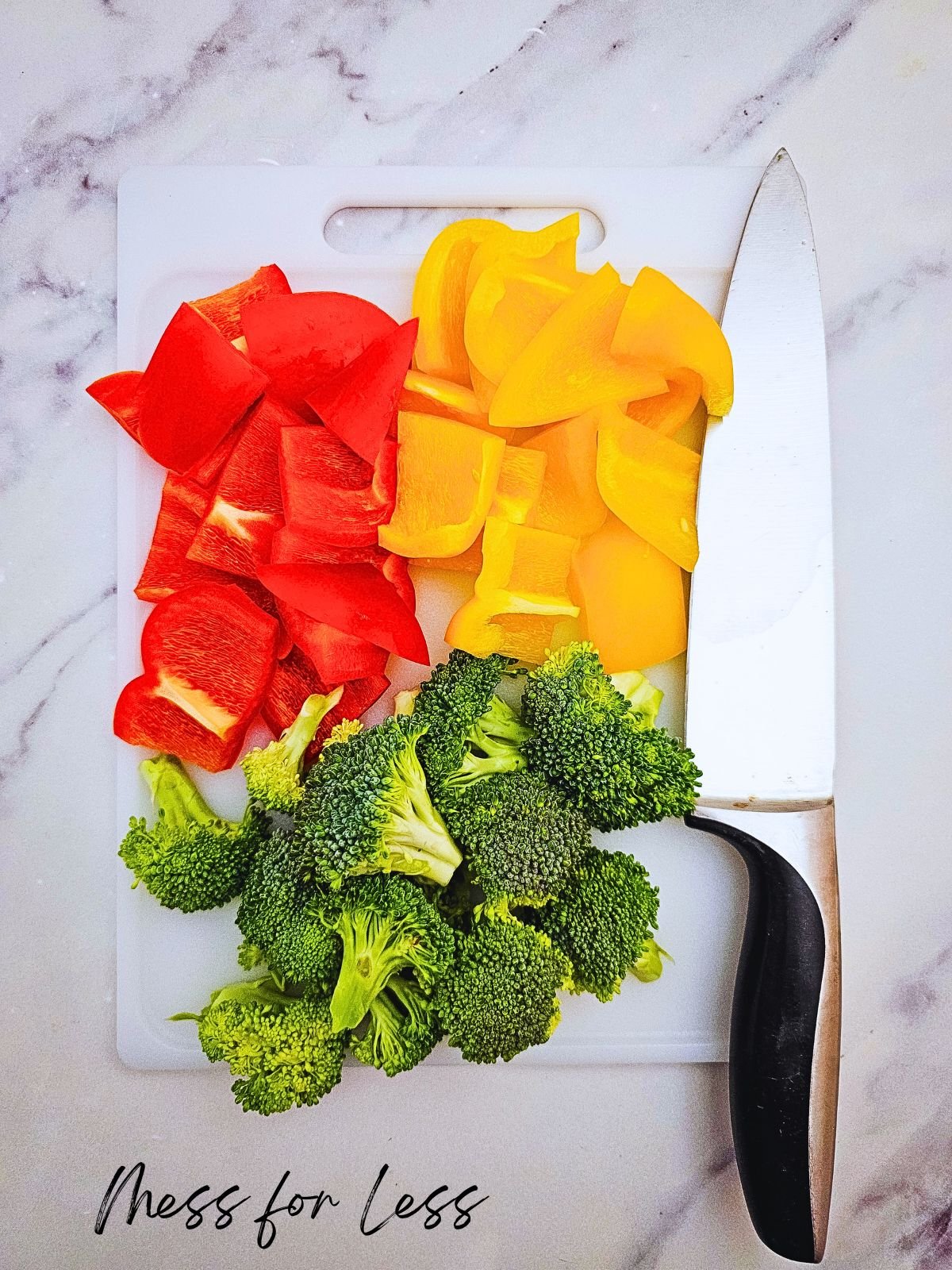 Chopped red and yellow bell peppers, broccoli, and sausage on a cutting board with a knife