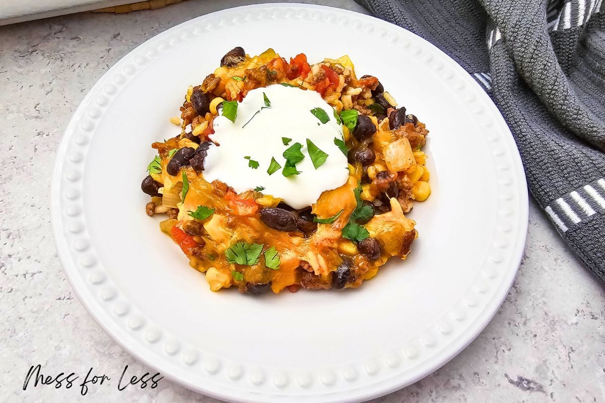 A plate of Taco Rice Casserole topped with sour cream and chopped herbs, served on a white dish.