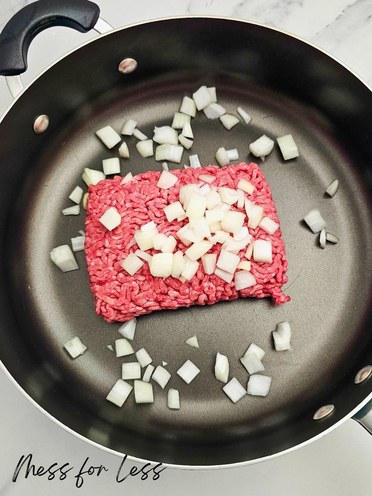 Ground beef and chopped onions in a black skillet, ready to be cooked for a delicious Taco Rice Casserole.