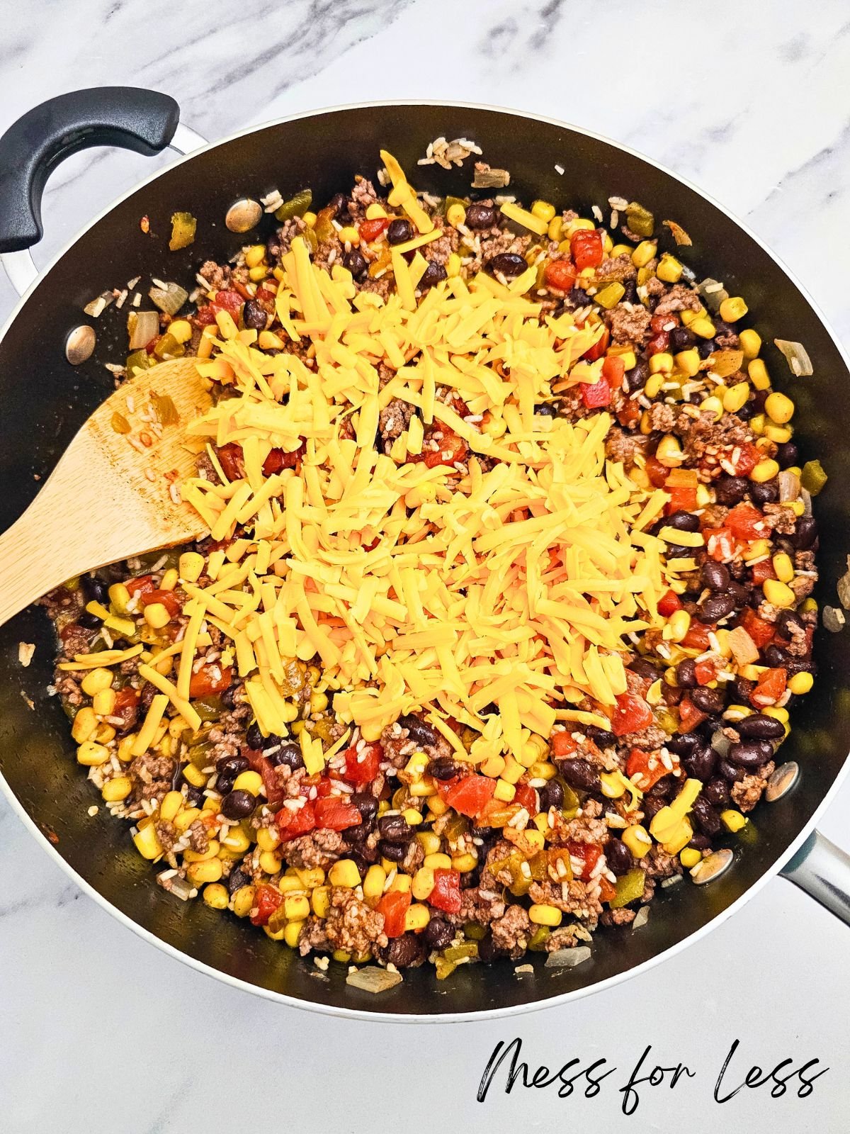 A skillet of Taco Rice Casserole with ground beef, beans, corn, tomatoes, and shredded cheese, served with a wooden spoon.