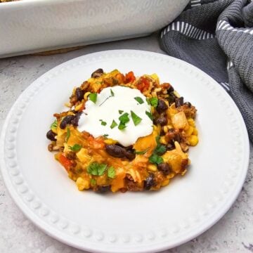 A serving of Taco Rice Casserole with black beans, vegetables, melted cheese, and sour cream, garnished with parsley.