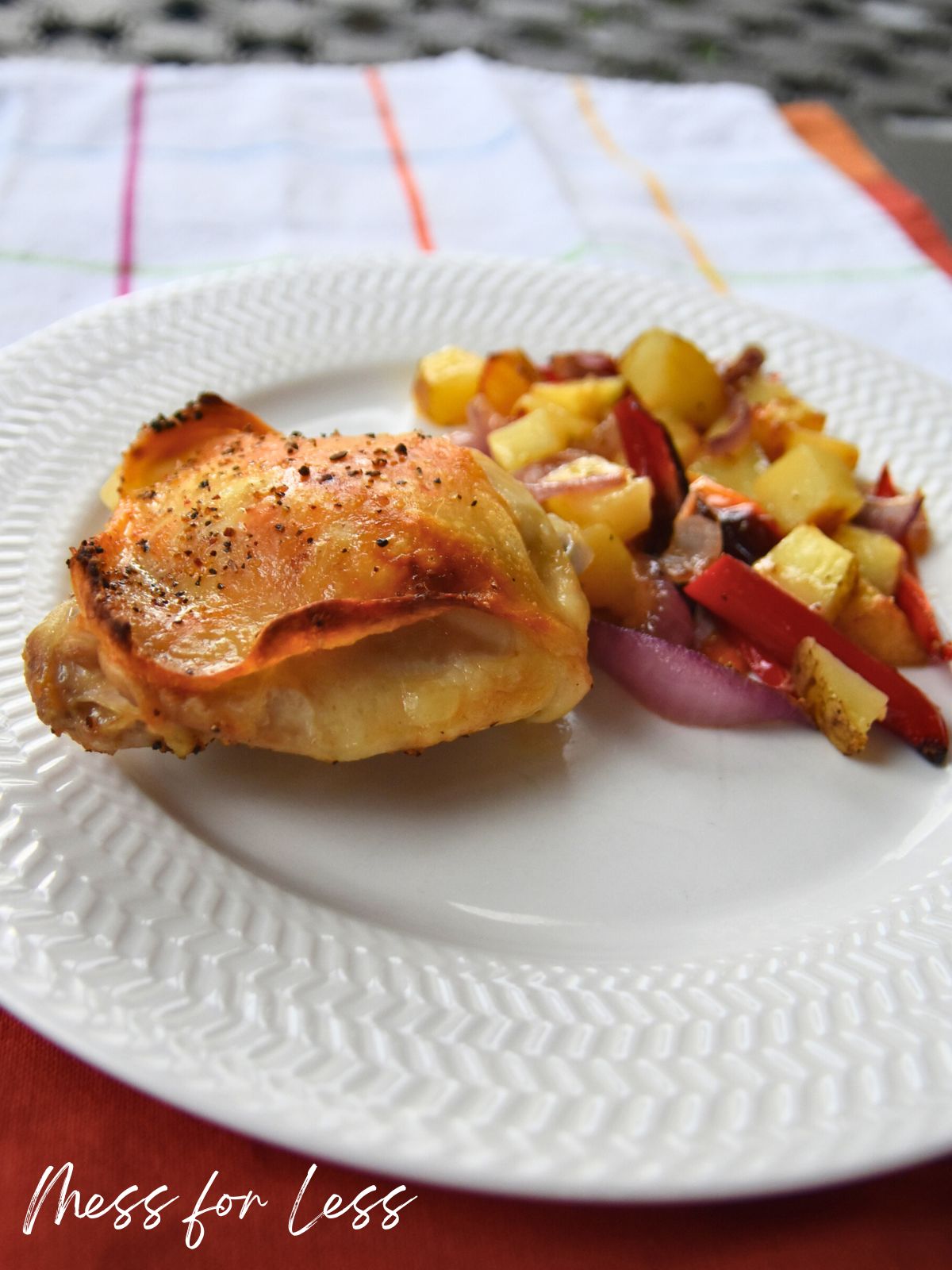 A plate with baked Sheet Pan Chicken Thighs and roasted vegetables, including potatoes, red onions, and peppers.